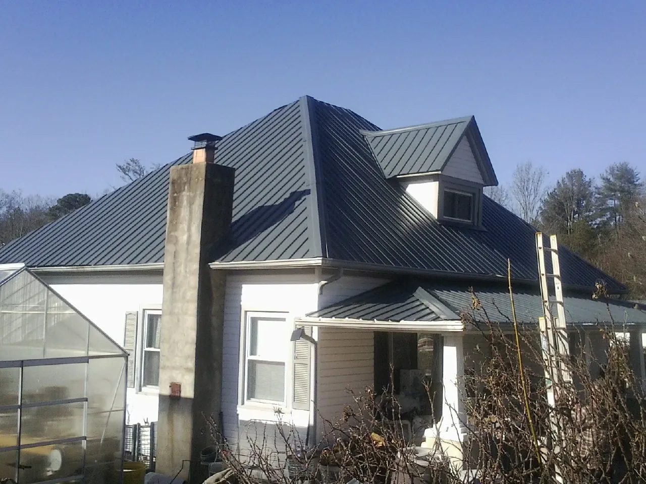 Dark blue standing seam metal roof on a white farmhouse with dormer — Slate & Tile Roof Repair by Roofing Brothers in Mc Queeney
