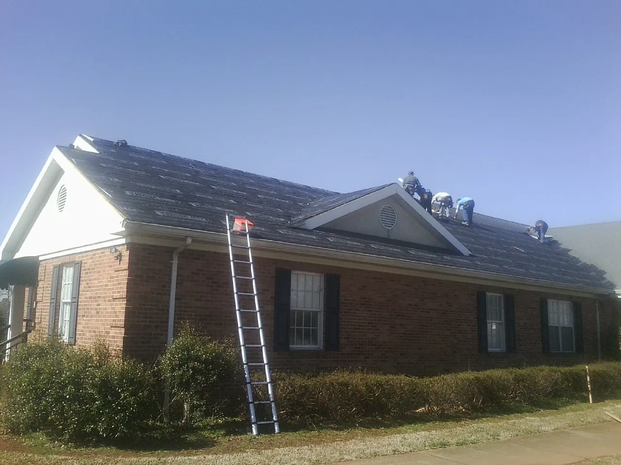 Crew tearing shingles off a brick ranch roof with a ladder set — Metal Roof Repair work by our crew in Mc Queeney