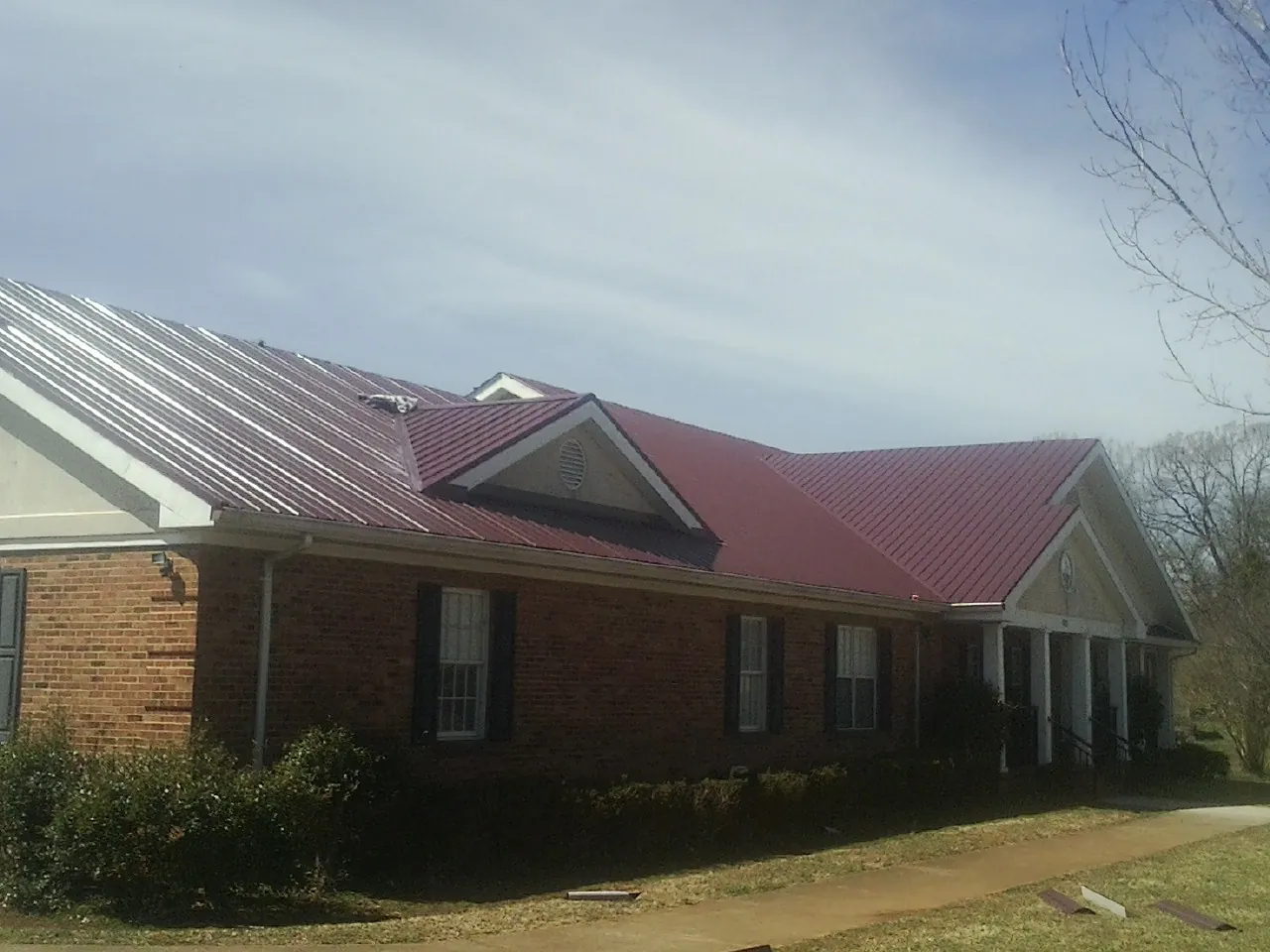Red metal roof with gabled entries on a long brick building, from a Hail Damage Roof Repair job in Mc Queeney