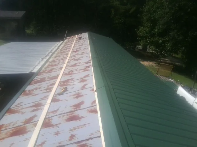 Old rusted panels beside newly installed green metal roofing — Wind Damage Roof Repair by Roofing Brothers in Mc Queeney