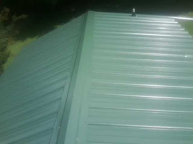 New green metal panels meeting at the ridge of a roof — Flat Roof Repair work by our crew in Mc Queeney