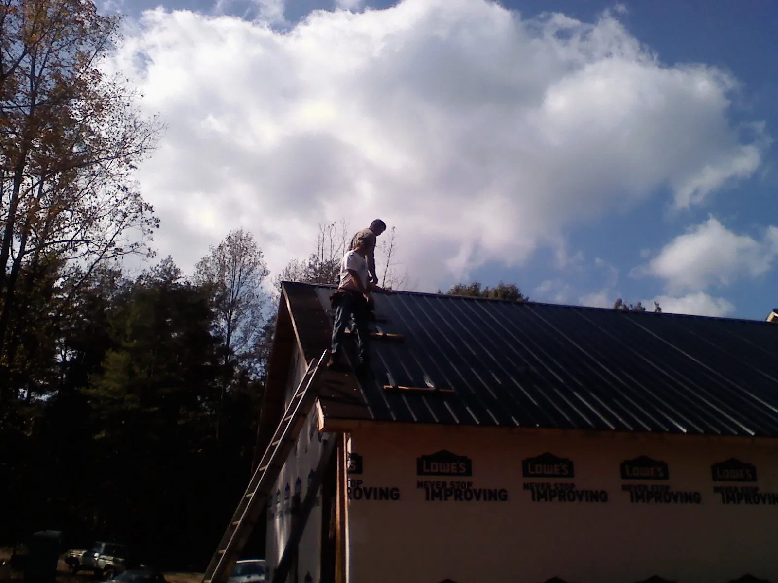 Roofer fastening dark metal panels high against a cloudy sky, from a Roof Inspection job in Mc Queeney