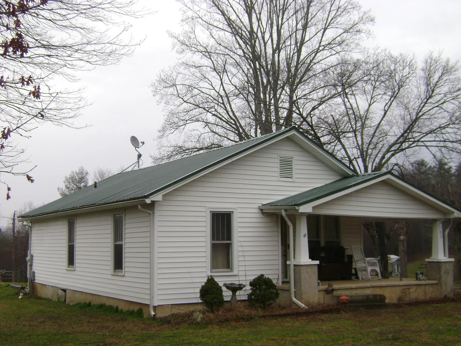 Green metal roof on a white bungalow with a side porch in Mc Queeney