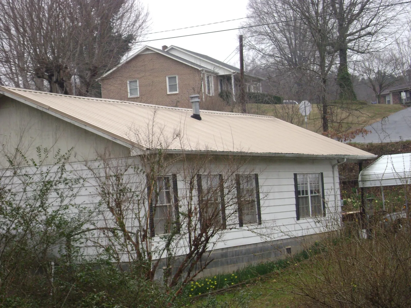 Tan metal roof on a white sided house set into a hillside — Commercial Roofing by Roofing Brothers in Mc Queeney